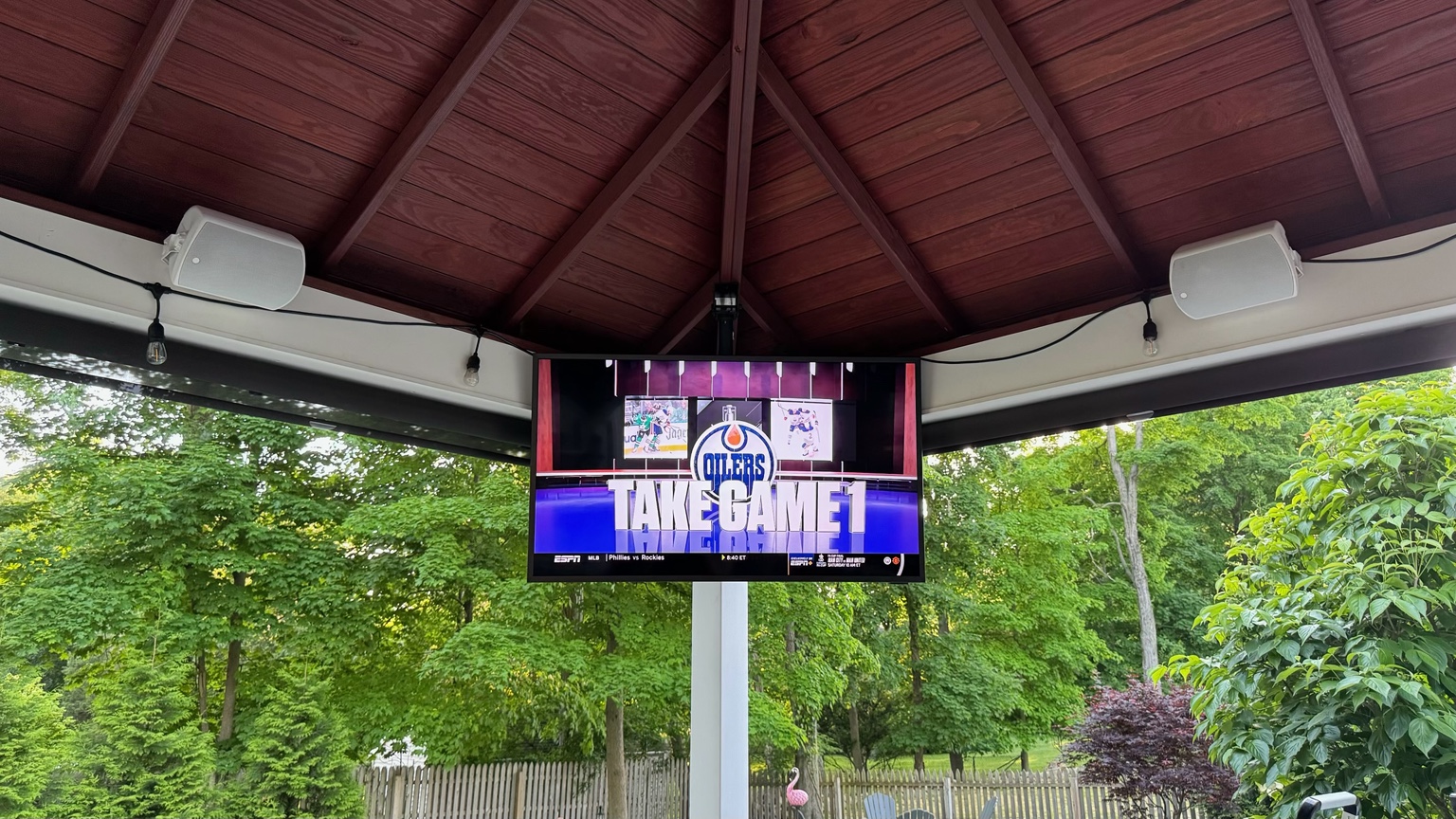 TV and two white speakers installed beneath a covered patio roof.